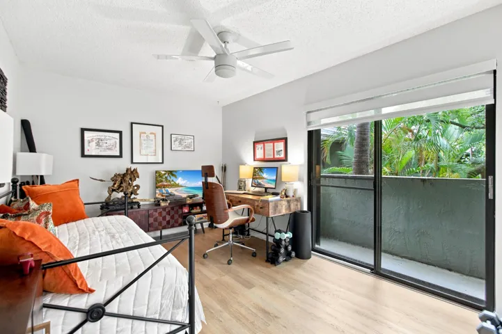 Light wood-finish flooring with a ceiling fan, sliding glass doors, and a private outdoor space featuring tropical foliage