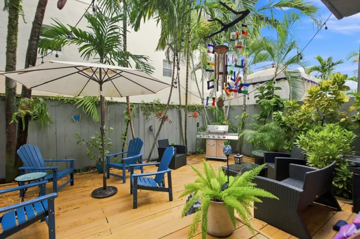 Expansive wood-finish deck with mature palm trees, perimeter fencing, string lighting, and built-in outdoor cooking station