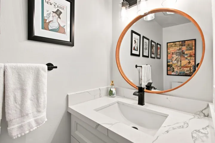 Bathroom vanity featuring a round framed mirror, a quartz countertop, an integrated sink, a matte black faucet, and a wall-mounted light fixture
