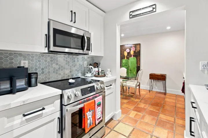 Modern kitchen featuring white shaker cabinetry, stainless steel appliances, a hexagonal tile backsplash, and light-colored countertops