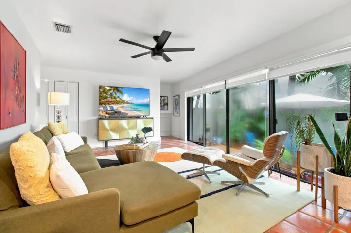 Living area featuring terra cotta tile flooring, a contemporary ceiling fan, and extensive sliding glass doors