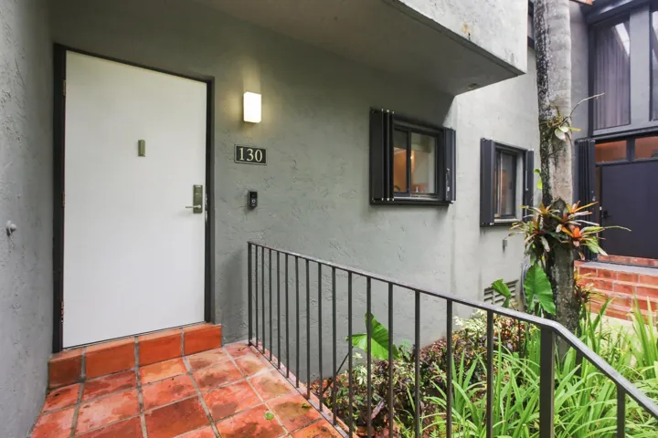 Entryway featuring terra cotta tile flooring, a white entry door with modern hardware, and a wall-mounted light fixture