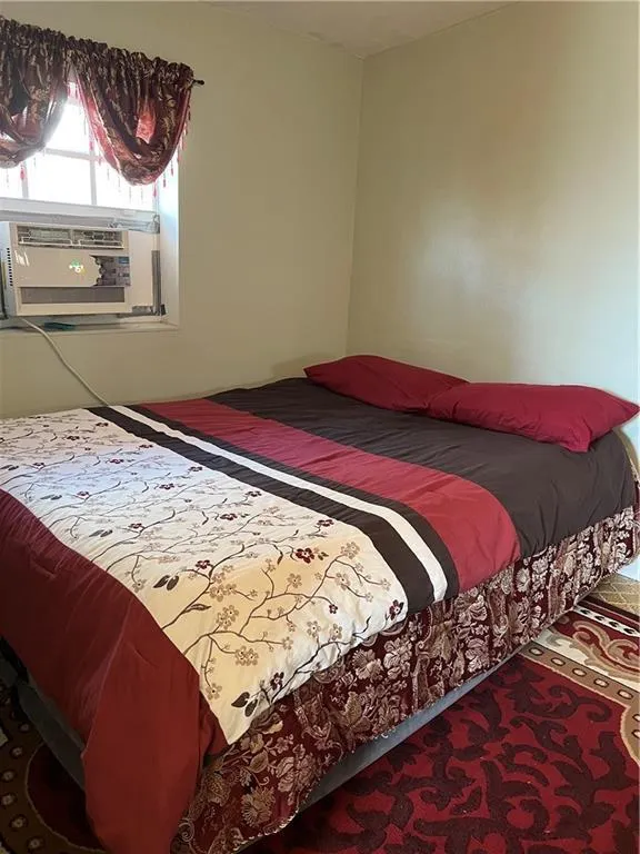 Bedroom featuring light-colored walls and a window with a built-in air conditioning unit