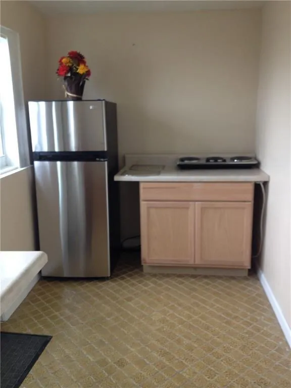 Compact kitchen area featuring a stainless steel refrigerator, light-toned cabinetry, and a countertop with a built-in cooktop