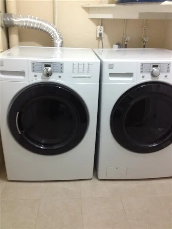 Laundry area featuring a side-by-side washer and dryer, light-toned wall paint, and a neutral tile floor