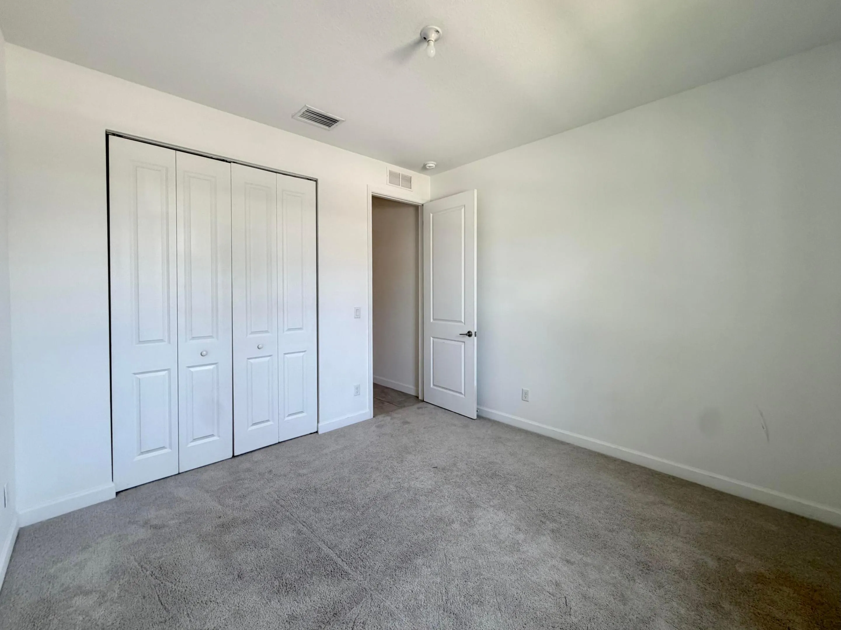 Neutral tone wall finishes, gray carpet flooring, white trim, white paneled bifold closet doors, and a white paneled interior door with black hardware