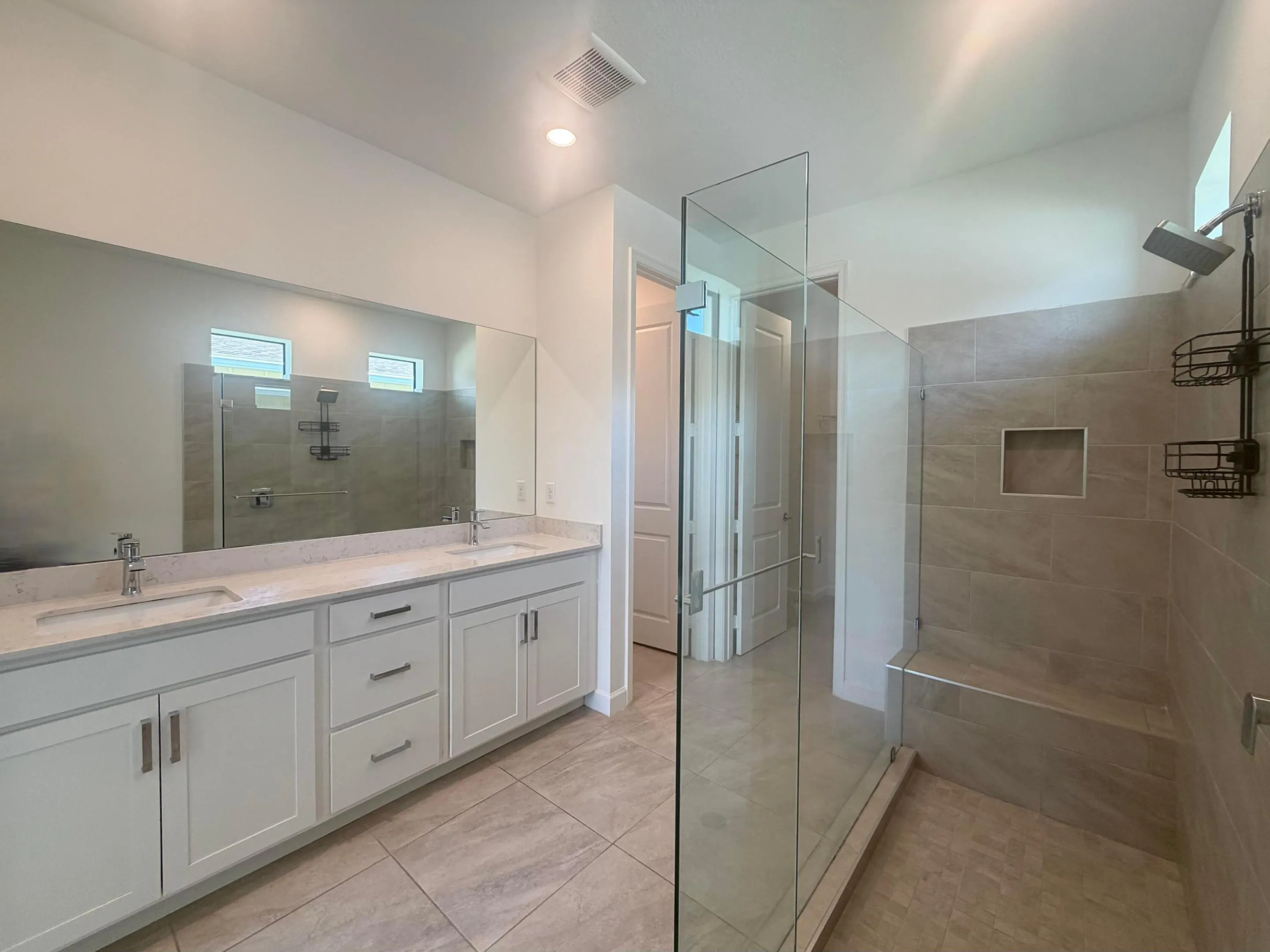 Expansive bathroom featuring a double vanity with stone countertops, a large glass-enclosed shower with a built-in bench, and tiled flooring