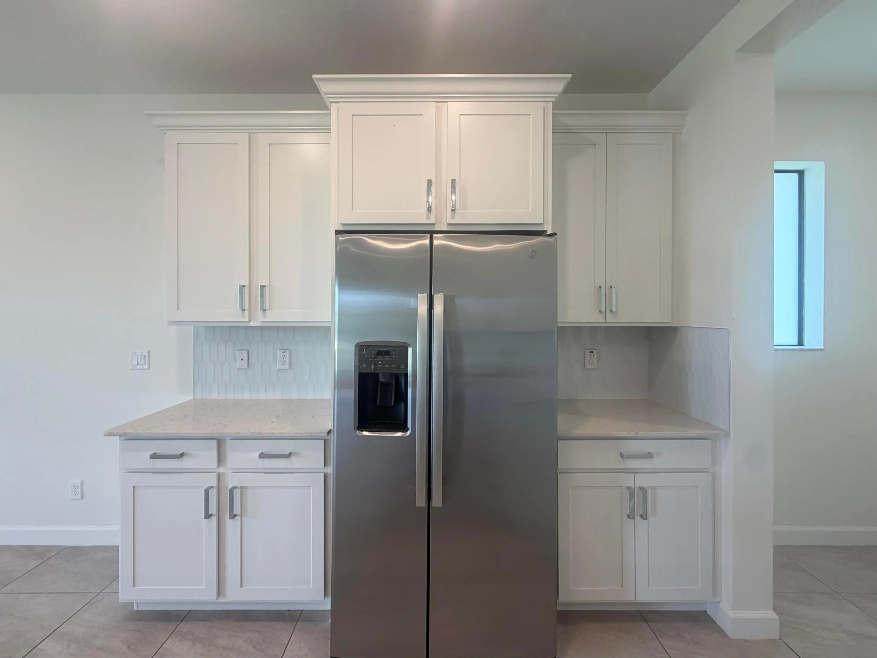 Stainless steel side-by-side refrigerator framed by white shaker-style cabinetry with crown molding