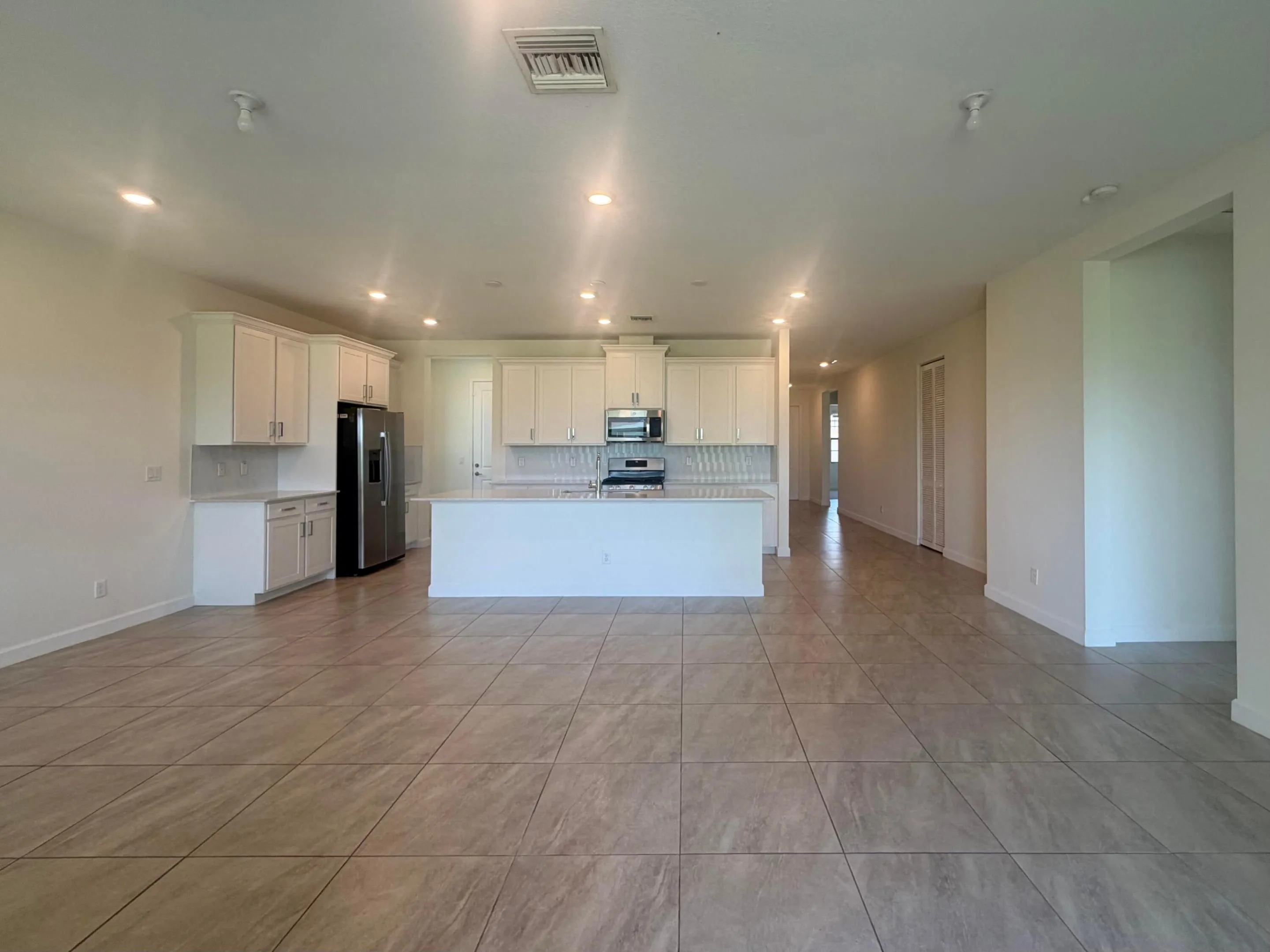 Open-concept kitchen and living area featuring tile flooring, white cabinetry, a large kitchen island, stainless steel appliances, and recessed lighting