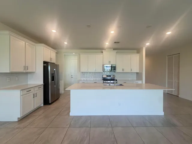 Spacious kitchen featuring white cabinetry with hardware accents, stainless steel appliances including a black refrigerator, and a large center island with white quartz countertop
