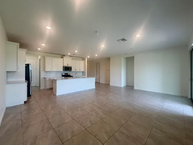 Open-concept living area featuring a kitchen with white cabinetry, a center island, stainless steel appliances, a tile backsplash, and light-toned tile flooring throughout