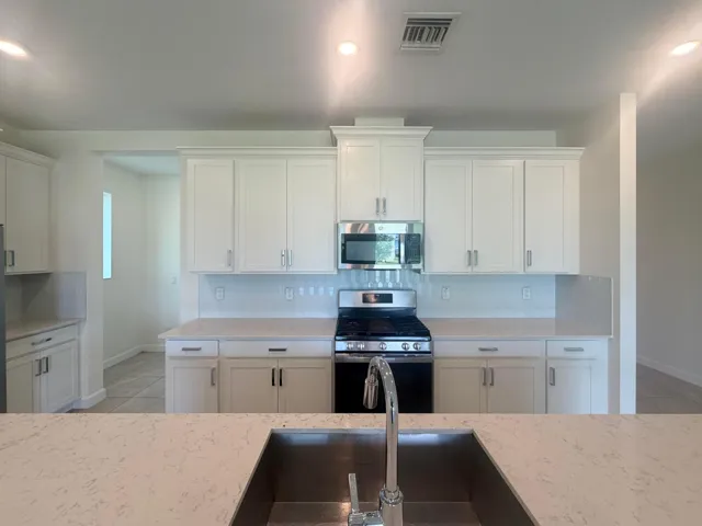 Kitchen featuring white shaker cabinetry, light-toned countertops, a subway tile backsplash, a stainless steel gas range, and an undermount stainless steel sink with a high-arch faucet