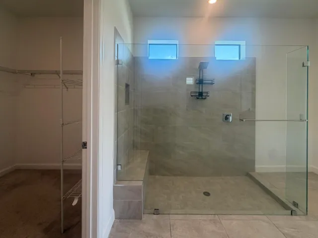Spacious walk-in shower with full glass enclosure, tiled walls, built-in bench, and rain shower head
