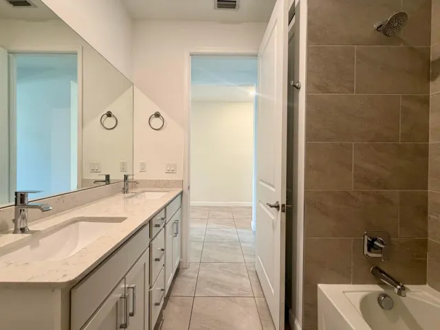 Contemporary bathroom featuring a dual vanity with undermount sinks, stone-finish countertop, and full-width mirror