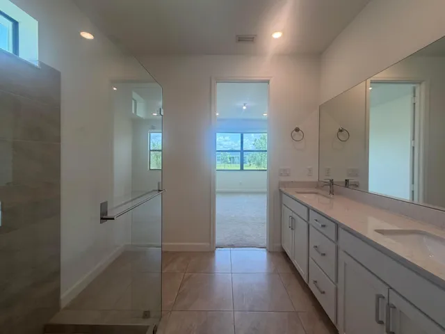 Spacious bathroom featuring a dual vanity with light-colored countertops, a large frameless mirror, and modern white cabinetry