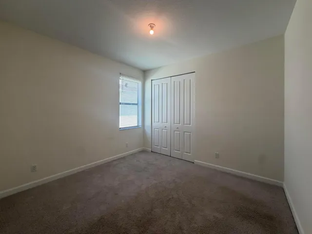 Bedroom featuring neutral wall paint, textured carpeting, a window with blinds, and bi-fold closet doors