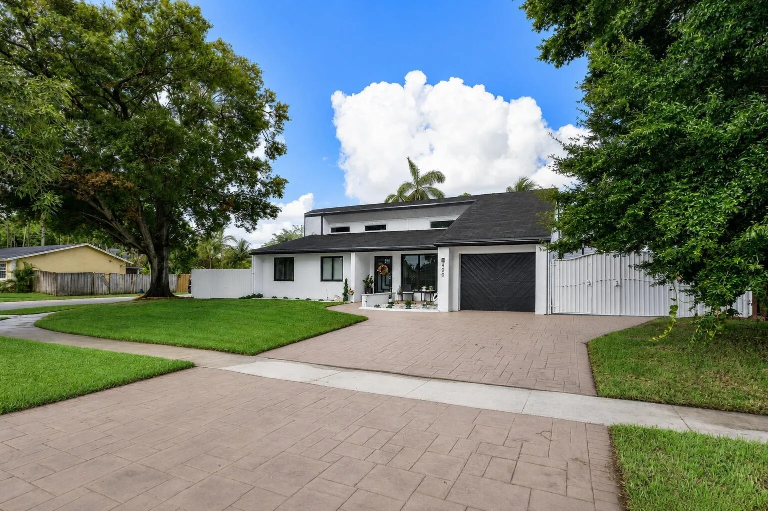 Contemporary residence featuring a white stucco facade, black shingle roofing, and a stamped concrete driveway