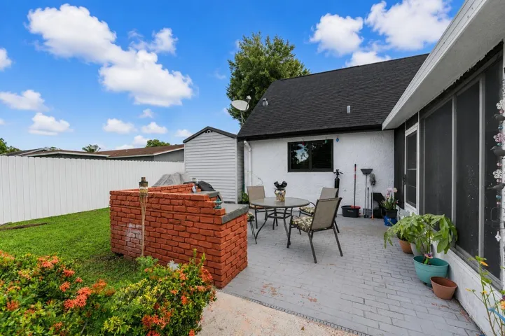 Expansive backyard featuring a brick built-in grill station, a paved patio, and a storage shed