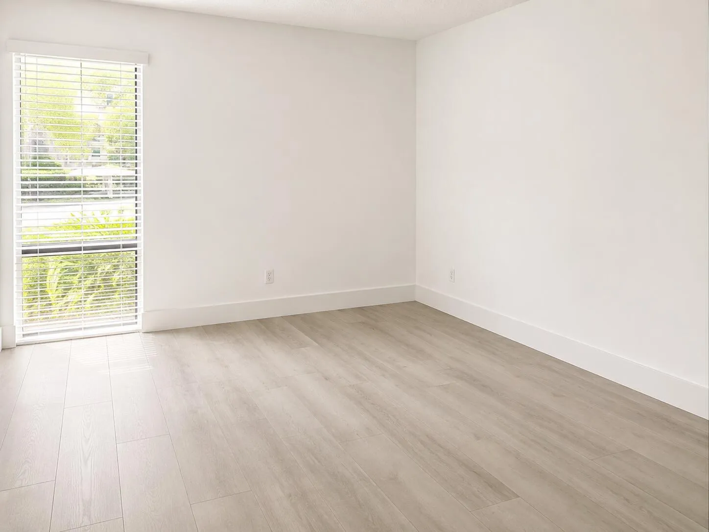 Bright room featuring light wood-finish flooring, white baseboards, and a large window with horizontal blinds