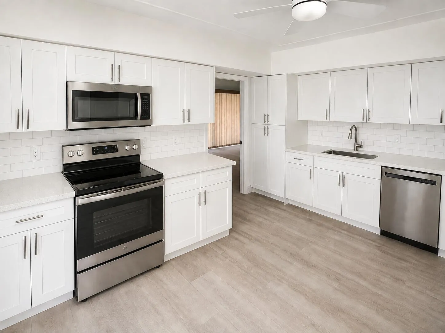 Bright kitchen featuring white shaker cabinetry, stainless steel appliances, light countertops, subway tile backsplash, and wood-finish flooring