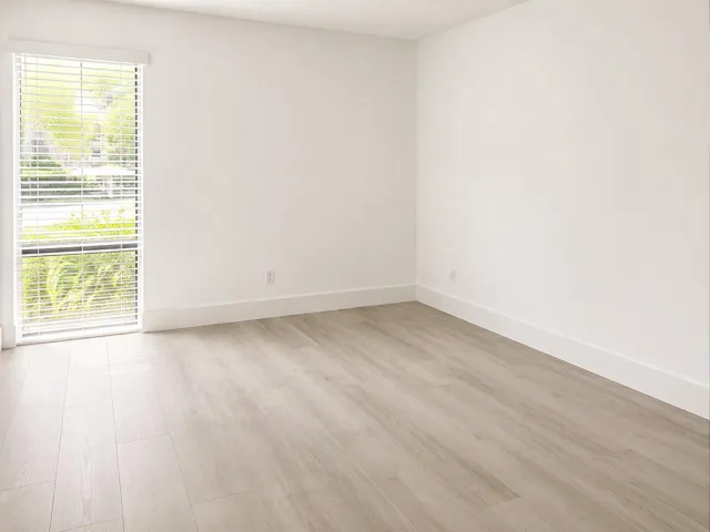 Bright room featuring light wood-finish flooring, white baseboards, and a large window with horizontal blinds