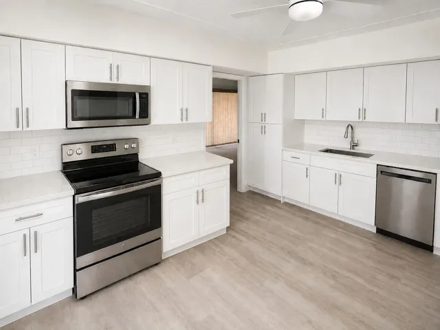 Bright kitchen featuring white shaker cabinetry, stainless steel appliances, light countertops, subway tile backsplash, and wood-finish flooring