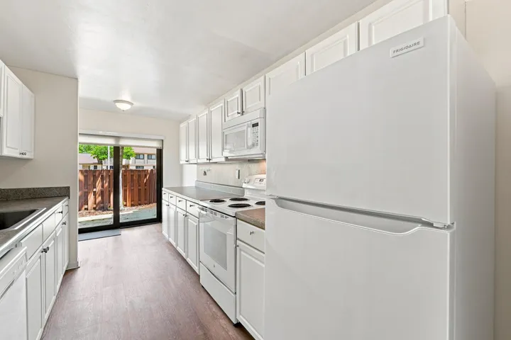 Kitchen featuring white cabinetry, wood-finish flooring, and white appliances