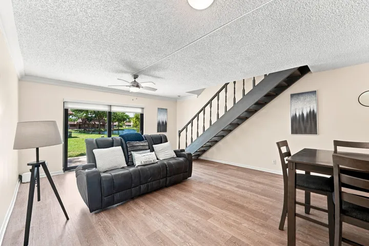 Wood-finish flooring, sliding glass door, ceiling fan, open-tread staircase with dark railings, and crown molding