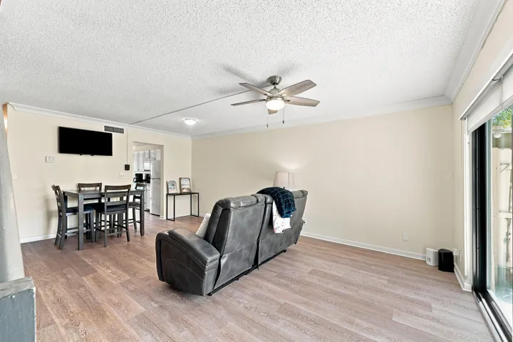 Wood-finish flooring, ceiling fan with integrated lighting, crown molding, and sliding glass door