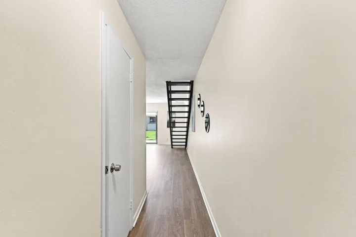 Hallway featuring wood-finish flooring, light-toned walls, and a black open-tread staircase