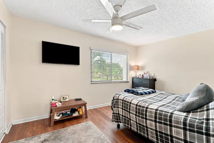 Wood-finish flooring, ceiling fan with integrated lighting, window with horizontal blinds, and a wall-mounted flat-screen display