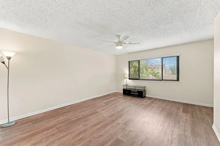Wood-finish flooring, neutral wall tones, window with horizontal blinds, and a ceiling fan with integrated lighting