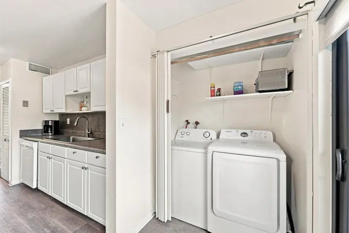 Compact kitchen featuring white cabinetry, a stainless steel sink with a high-arc faucet, and dark countertops