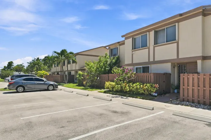 Two-story townhome with neutral stucco exterior, prominent second-story windows, and a private fenced front yard