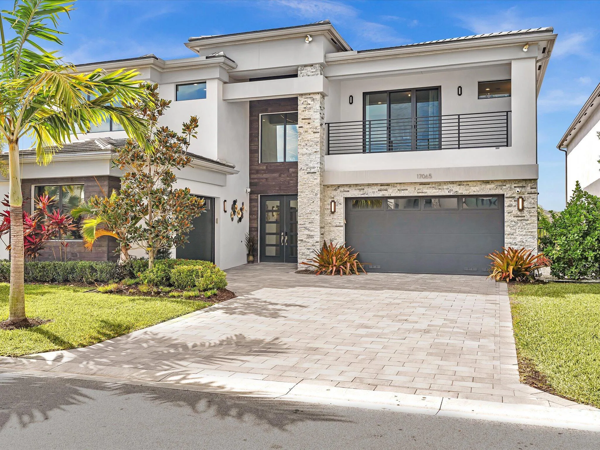 Modern elevation with clean architectural lines, lush landscaping, and an oversized paver driveway creating striking curb appeal.