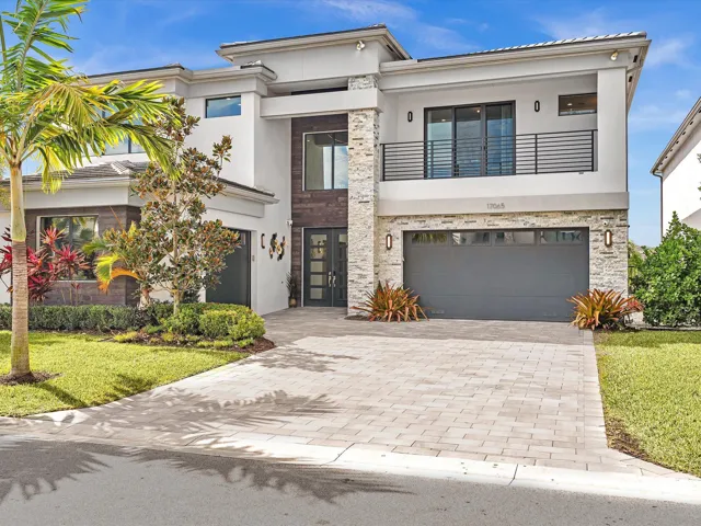 Modern elevation with clean architectural lines, lush landscaping, and an oversized paver driveway creating striking curb appeal.
