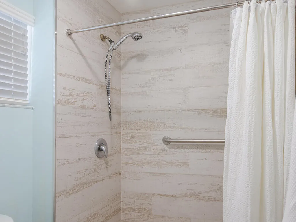 Shower enclosure featuring wood-look tile surround, brushed nickel fixtures, a handheld showerhead, and a grab bar