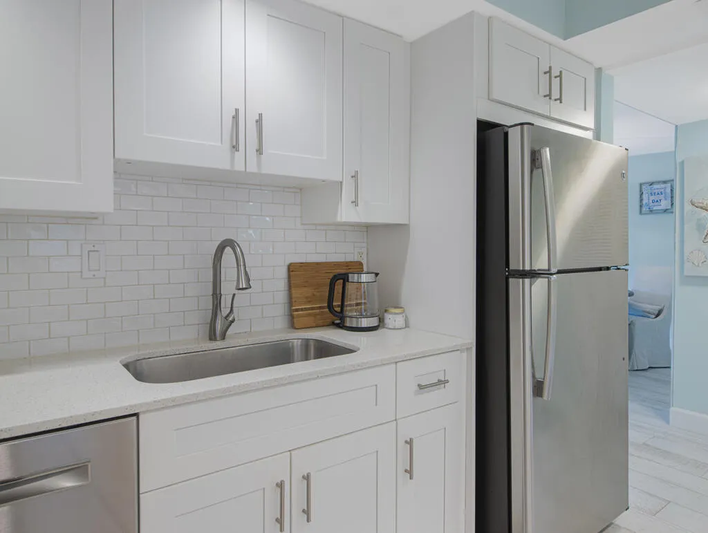 Contemporary kitchen featuring white shaker cabinetry, stainless steel appliances, a subway tile backsplash, light-toned countertops, and an undermount sink with a gooseneck faucet