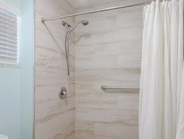 Shower enclosure featuring wood-look tile surround, brushed nickel fixtures, a handheld showerhead, and a grab bar