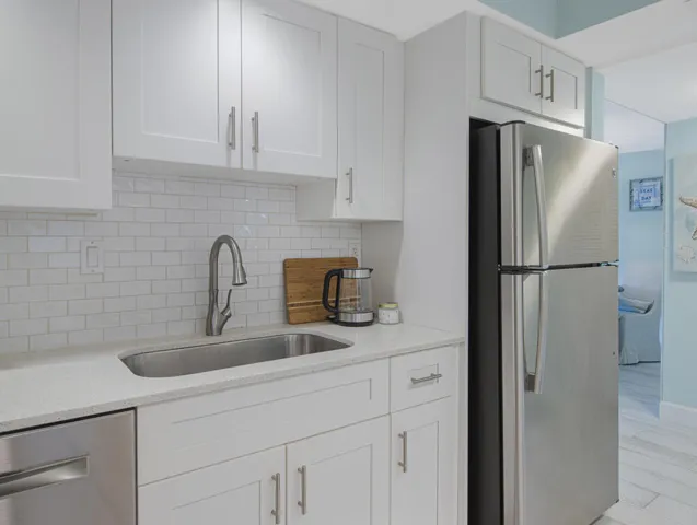 Contemporary kitchen featuring white shaker cabinetry, stainless steel appliances, a subway tile backsplash, light-toned countertops, and an undermount sink with a gooseneck faucet
