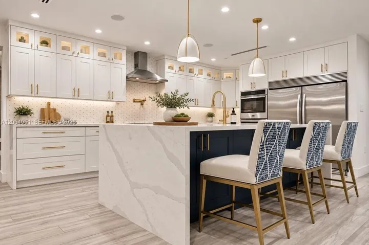 Kitchen featuring a center island with a waterfall countertop, white shaker-style cabinetry with glass-front uppers, stainless steel professional-grade appliances, patterned tile backsplash, and recessed lighting