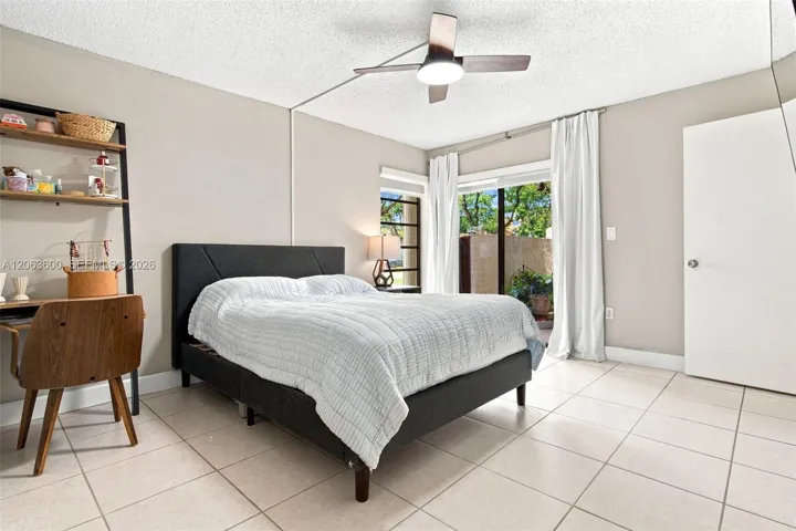 Primary bedroom with tile flooring, sliding glass door to a private exterior patio, and natural light from a corner window.