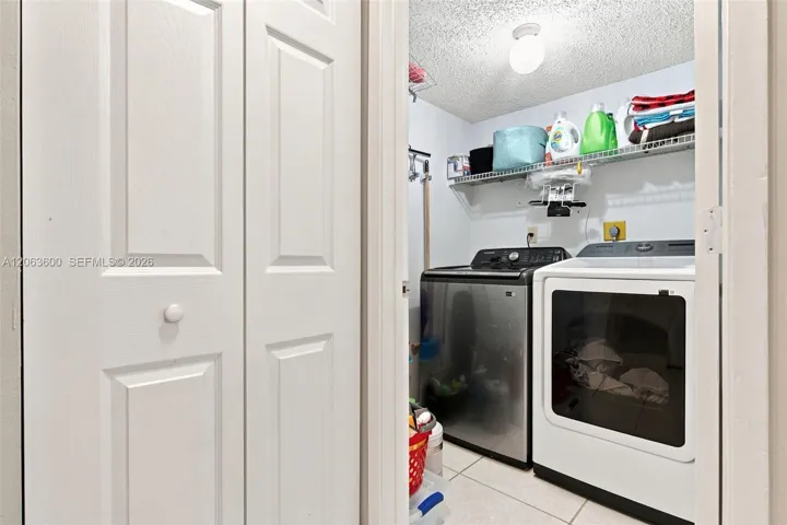 In-unit laundry closet with full-size Samsung washer and dryer, plus overhead wire shelving for storage.