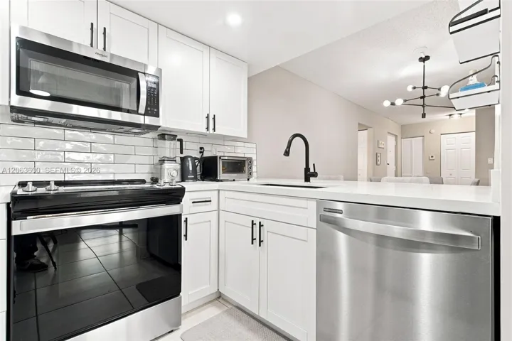 Kitchen with white cabinetry, subway tile backsplash, gas range, stainless steel dishwasher, and black matte fixtures; open sightline to the dining area beyond.
