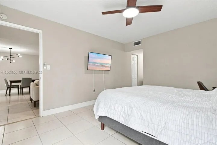 Primary bedroom with tile flooring, wall-mounted TV, and pass-through to the dining area.