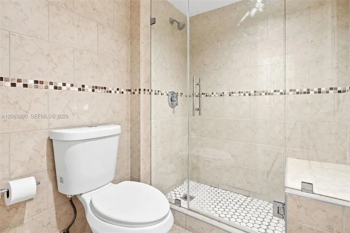 Remodeled shower with floor-to-ceiling tile, mosaic tile accent band, glass enclosure, and penny-tile shower floor.
