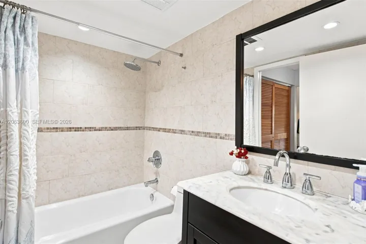 Full bathroom with marble-look tile surround, tub/shower combo with rain showerhead, and dark wood vanity with marble countertop.
