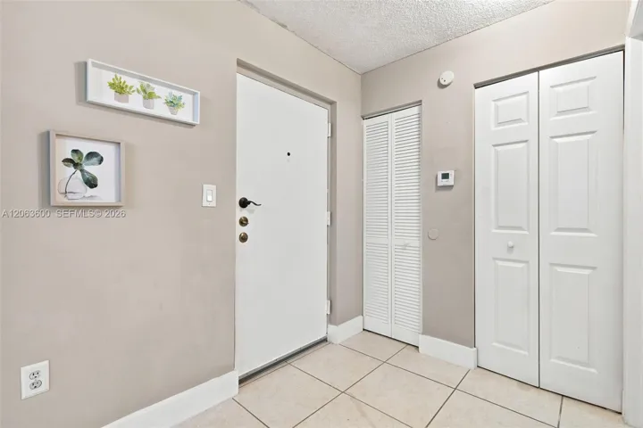 Foyer with tile flooring, coat closet, and additional storage closet with louvered doors beside the entry.