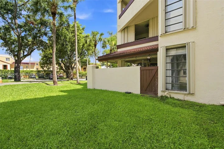 Ground-level exterior view showing the covered patio, mature palm trees, and manicured lawn along the building's side yard.