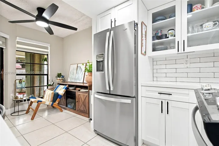 Kitchen corner with white shaker cabinetry, subway tile backsplash, quartz countertops, stainless steel French-door refrigerator, and glass-front upper cabinet display shelving.